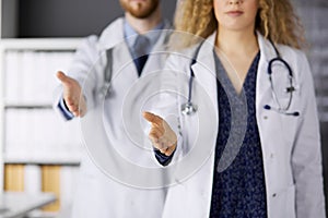 Two doctors standing and offering helping hand for shaking hand or saving life. Medical help, countering viral infection