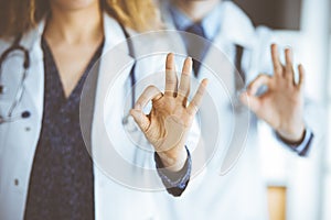 Two doctors standing with Ok sign in hospital office. Medical help, countering viral infection and medicine concept