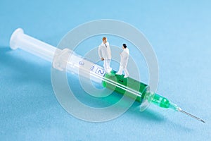 Two doctors standing on a syringe with green fluid in it