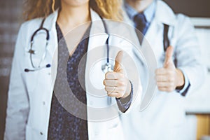 Two doctors standing with thumbs up in hospital office. Medical help, countering viral infection and medicine concept