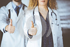 Two doctors standing with thumbs up in hospital office. Medical help, countering viral infection and medicine concept