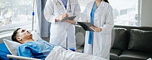 Two doctors talking to a patient lying in his bed with receiving saline solution in hospital