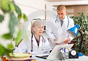 Two doctors working with patient records on laptop in medical office