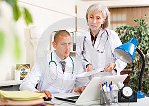 Two doctors working with patient records on laptop in medical office