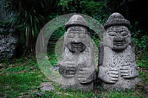 Two Dol Hareubang statues in dark green forest, Seogwipo, Jeju Island, South Korea