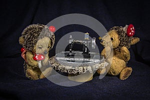 Two dolls of hedgehogs-tailors, sitting at the table with a sewing machine