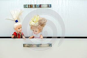 Two dolls sitting in a cabinet drawer in nursery playroom. Lot of toys in children`s room