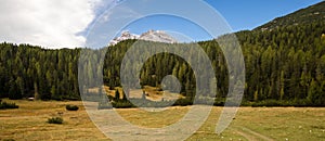 Two Dolomites` peaks appear above coniferous forest, tempting walkers onwards