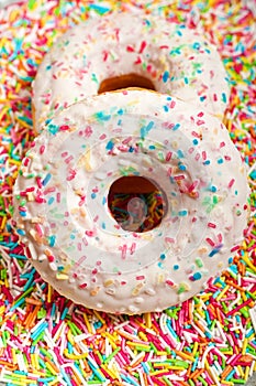 Two donuts with colorful sprinkles and glazes surface over colorful background