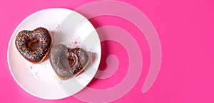 two donuts in a heartshape on a white plate and on a pink background. Concept for Valentine's Day. Valentine's