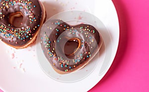 two donuts in a heartshape on a white plate and on a pink background. Concept for Valentine's Day. Valentine's