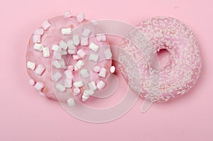 Two donuts with icing on pastel pink background. Copyspace