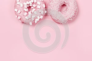 Two donuts with icing on pastel pink background. Copyspace