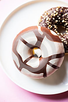 Two doughnuts with chocolate glaze and peanuts on a pink background. Close up