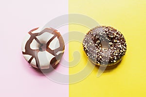 Two doughnuts with chocolate glaze on a pink and yellow background. Top view