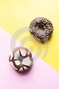 Two doughnuts with chocolate glaze on a pink and yellow background. Top view