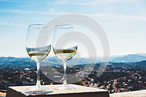 Two drink glass white wine standing on background blue sea top view city coast yacht from observation deck, romantic toast with al