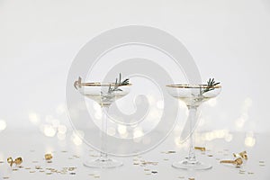 Two drinking glasses with champagne, bubbly wine. White table. Golden star shape confetti. Blurred background with bokeh