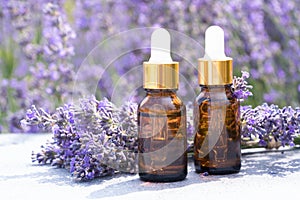 Two dropper bottles with lavender cosmetic oil or face serum against lavender flowers field as background