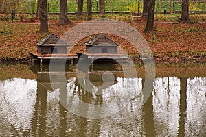 Two duck houses near a pond in Zamosc city park. Autumn landscape