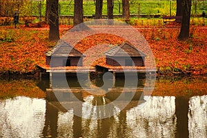 Two duck houses near a pond in Zamosc city park. Autumn landscape