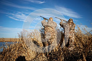 Two duck hunters shooting into sky with rifles