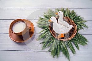 Two duck shaped ginger cookies with basket nest wreath with spikelets top view with tea cup on a white wooden background.