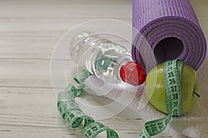 Two dumbbells, bottle of water, green apple, centimeter on white