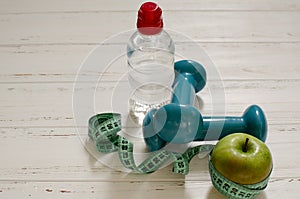 Two dumbbells, bottle of water, green apple, centimeter on white