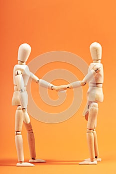 Two dummies shaking hands closing a deal on an orange background