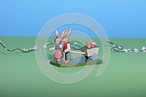 Two easterbunnies pull a cart with coloured eggs