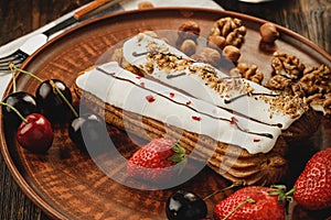 Two eclairs decorated with berries and nuts