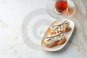 Two eclairs with white custard on whhite plate close up