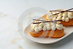 Two eclairs with white custard on whhite plate close up photo