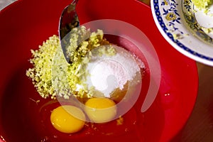 Two egg yolks with white yellow sugar oil and lemon peel in a red bowl for cake preparation