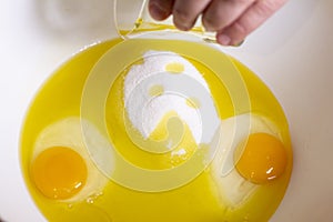 Two egg yolks with yellow white and sugar and oil in a red bowl for cake preparation