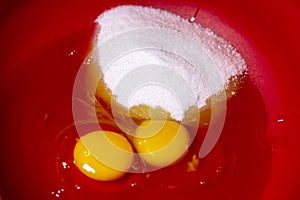 Two egg yolks with yellow white and sugar and oil in a red bowl for cake preparation