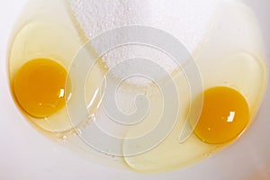 Two egg yolks with yellow white and sugar in a red bowl for cake preparation