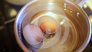 Two eggs boiling in hot water in a cooking pot on gas stove