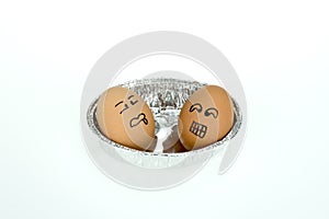 Two eggs with funny faces on oval foil tray, isolated on white background