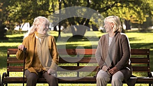 Two elderly ladies laughing and talking, sitting on bench in park, old friends