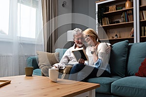 Two elderly people senior couple man and woman looking at a family photo smile and hug while sitting at home on sofa. memories and