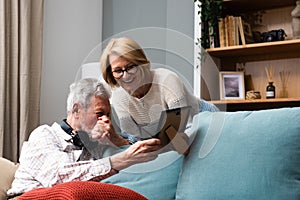 Two elderly people senior couple man and woman looking at a family photo smile and hug while sitting at home on sofa. memories and