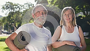 Two Elderly People Stand In Park With Sports Mats In Their Hands. They Talk Nicely.