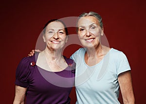 Two elderly women friends hugging on red background. Lifestyle and old people concept.