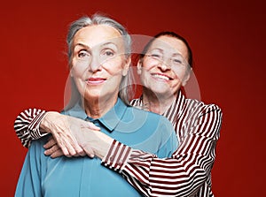 Two elderly women friends hugging on red background.