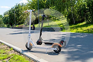 Two electric scooters, white and black, stand on the bandwagon on the street. Sunny summer day. Modern city transport.