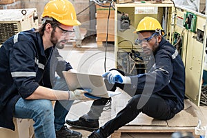 Two electricians engineer using laptop repairing electricity power in control cabinet at factory