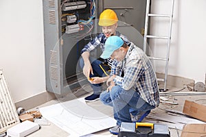 Two electricians with house plan near distribution board indoors