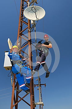 Two electricians in protective workwear install telecommunications antenna system